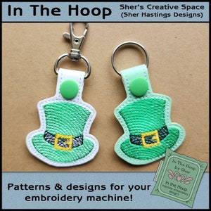 May include: Two green and white embroidered leprechaun hats with gold buckles, attached to key rings. The hats are on a brown background with the text "In The Hoop by Sher" and "In the Hoop machine embroidery designs".