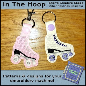 Puede incluir: Dos llaveros de patines de ruedas bordados, uno rosa y otro blanco, con ruedas moradas. Los llaveros están unidos a llaveros plateados. La imagen está sobre un fondo de madera con el texto "In The Hoop by Sher" y "Patrones y diseños para tu máquina de bordar!"