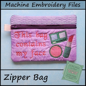 May include: A lavender quilted zipper bag with the text "This bag contains my face" embroidered in red. The bag features embroidered makeup items: eyeshadow, lipstick, and blush. The top has a quilted pattern and a zipper closure.