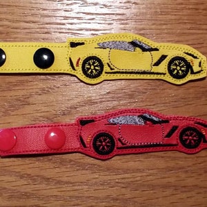 May include: Two fabric mask extenders with a car design. The top extender is yellow with black buttons and the bottom extender is red with red buttons.