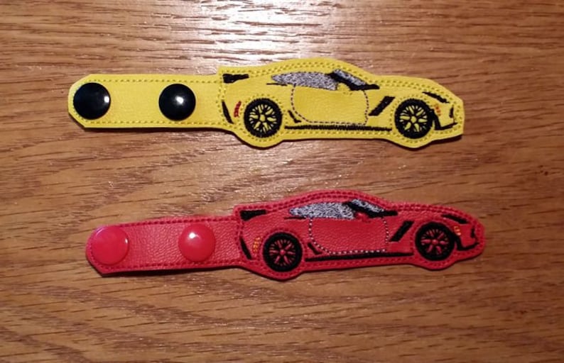 May include: Two fabric mask extenders with a car design. The top extender is yellow with black buttons and the bottom extender is red with red buttons.