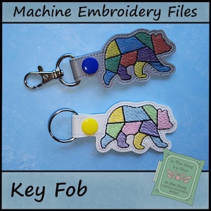 May include: Two key fobs with a bear design. The bears are made of colorful geometric shapes and have a metal clasp and key ring. The text "Machine Embroidery Files" and "Key Fob" are visible.