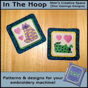 May include: Two embroidered designs featuring cats with hearts. The designs are on a blue background with a green border. The text "In The Hoop by Sher" is visible in the lower right corner.