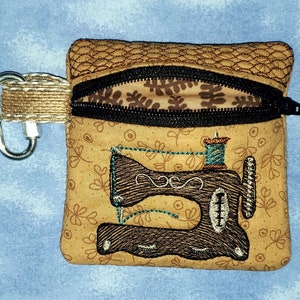 May include: A small brown zippered pouch with a brown and black sewing machine design. The pouch has a brown and black zipper and a silver carabiner clip.