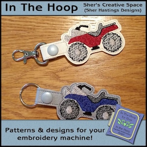 Puede incluir: Dos llaveros bordados con un ATV rojo y azul con contornos negros. Los llaveros están unidos a correas de cuero blanco con llaveros plateados. El texto "In The Hoop by Sher" es visible en la esquina inferior derecha de la imagen.