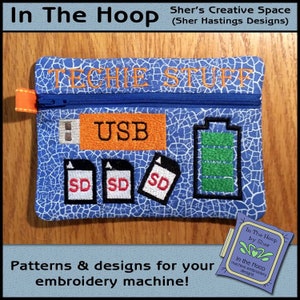 May include: Blue zippered pouch with "TECHIE STUFF" embroidered on the front. Features a USB symbol, SD card icons, and a battery indicator. The pouch has an orange zipper pull and is designed for embroidery machines.