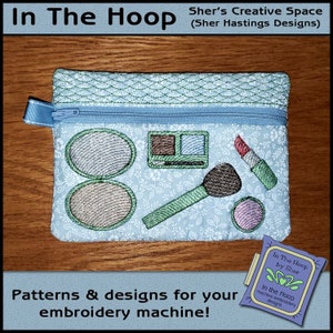 May include: A light blue zippered pouch with a floral pattern. The pouch has embroidered images of makeup items, including eyeshadow palettes, blush, lipstick, and a makeup brush. The text "In The Hoop by Sher" is visible on a small tag.