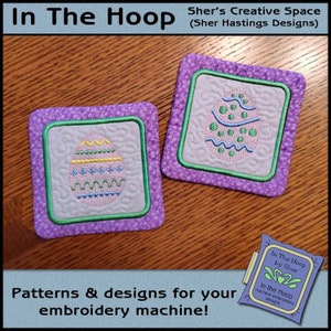 Puede incluir: Dos posavasos bordados con diseños de huevos de Pascua. Los posavasos son cuadrados y tienen una tela morada con un borde verde. Los huevos están bordados en hilo rosa, azul, verde y amarillo. El texto "In The Hoop by Sher" es visible en la esquina inferior derecha de la imagen.