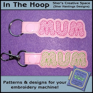 May include: Two pink and green embroidered keychains with the word "MUM" on them. The keychains are on a purple background. The text "In The Hoop by Sher" is visible in the bottom right corner of the image.