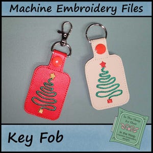 May include: Two key fobs with Christmas tree designs. One is red with a green tree and gold star, the other is off-white with a green tree and red star. Both have metal key rings and red snap closures.