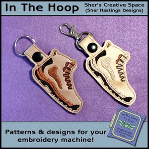 May include: Two embroidered boot keychains with brown and beige stitching on a light purple background. The text "In The Hoop by Sher" is visible in the lower right corner of the image.