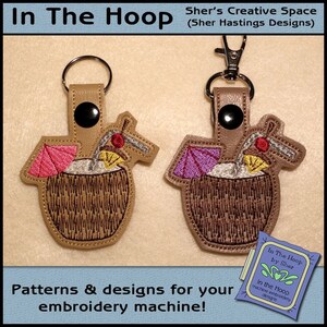 May include: Two brown leather keychains with embroidered images of a coconut drink with a straw and an umbrella. The text "In The Hoop by Sher" is visible on a small tag.