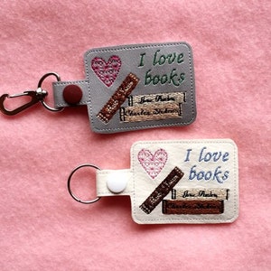 May include: Two keychains with a gray and white background. Both keychains feature a heart, stacked books, and the text "I love books".