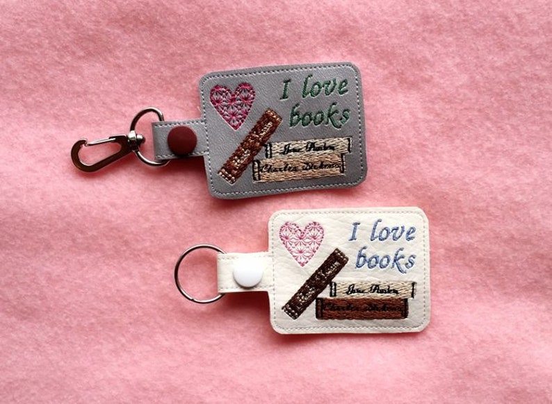 May include: Two keychains with a gray and white background. Both keychains feature a heart, stacked books, and the text "I love books".