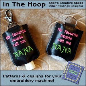 May include: Two black hand sanitizer holders with keychains. The holders are embroidered with the text "My favorite people call me Nana" in pink and green thread. The text "In The Hoop by Sher" is visible in the bottom right corner of the image.
