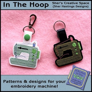 Puede incluir: Dos llaveros de máquina de coser, uno verde y otro dorado, con correas de cuero negro y anillos de llaves plateados. Los llaveros están sobre una superficie rosa y peluda. El texto "In The Hoop by Sher" está en la esquina inferior derecha de la imagen.