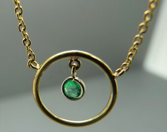 May include: A gold chain necklace with a circular pendant. The pendant has a small green emerald gemstone hanging from it.