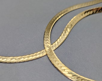 May include: Two gold snake chains, one on top of the other, with a textured, woven design.