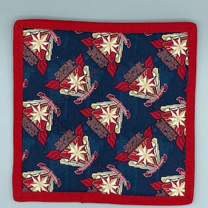 May include: Square Captain Marvel fabric item with a red border. The navy blue fabric features a repeating pattern of the Captain Marvel logo in red, gold, and white. The text "CAPTAIN MARVEL" is visible on the design.
