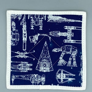 May include: Square navy blue fabric with a white border, featuring a blueprint design of various space vehicles. The design includes detailed illustrations of starfighters, walkers, and other spacecraft, creating a thematic pattern.