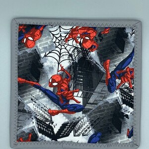 Puede incluir: Artículo de tela cuadrada con un patrón repetido de Spider-Man en poses de acción. El diseño incluye un fondo de paisaje urbano, una telaraña y un borde gris con bordes cosidos. El superhéroe está representado en su clásico traje rojo y azul.