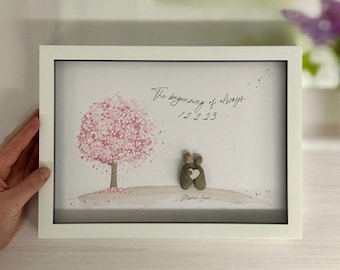 May include: A framed pebble art piece with a pink tree and two figures holding a heart. The text reads "The beginning of always 12.2.23".
