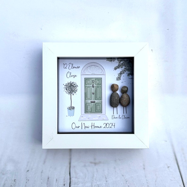 Puede incluir: Una imagen enmarcada en blanco con una ilustraci&oacute;n pintada a mano de una puerta verde con el n&uacute;mero de casa "12" y la direcci&oacute;n "12 Elmer Close". Dos personas de guijarros se paran frente a la puerta con el texto "Dave & Claire" debajo. El texto "Our New Home 2024" est&aacute; en la parte inferior de la imagen.