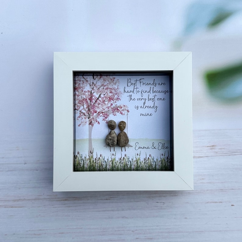 May include: White framed artwork with a pink tree and two pebble people sitting on a swing. The text reads "Best Friends are hard to find because The very best one is already mine" and is signed "Emma & Ellie".