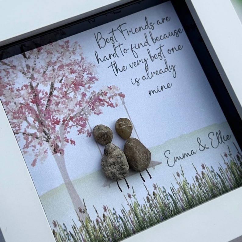 May include: A framed print with a watercolor painting of a tree with pink blossoms. The print has the text "Best Friends are hard to find because the very best one is already mine" and the names "Emma & Ellie".  There are four small gray stones arranged to look like two figures sitting on a swing.