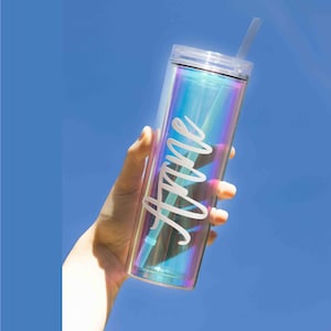 May include: A clear iridescent tumbler with a white straw and the name "Anne" written on the side. The tumbler is being held by a hand against a blue sky background.