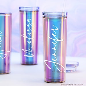 May include: Three iridescent tumblers with personalised names in white vinyl. The names are "Jennifer", "Melissa", and "Holly". The tumblers are made of clear plastic with a holographic finish. Blossom font, white vinyl.