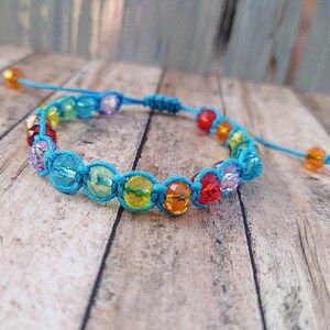 May include: A bracelet featuring a series of multi-colored, faceted, translucent beads in shades of red, orange, yellow, green, blue, and purple, held together by a bright turquoise cord with an adjustable sliding knot closure and two dangling beads.