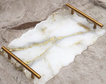 May include: White serving tray with gold accents and two gold metal handles. The tray has an irregular, organic shape.