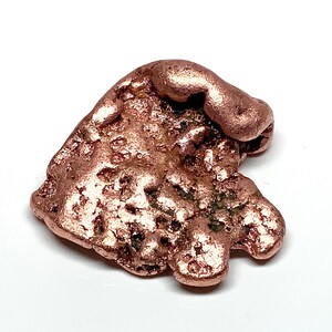 May include: A raw copper nugget with a metallic, reddish-brown luster. The surface is highly textured, featuring irregular bumps, crevices, and a porous, uneven appearance. The shape is asymmetrical with rounded edges and a dense, solid form.