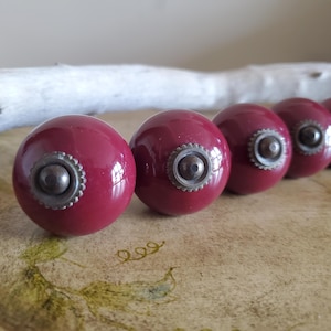 May include: Six red ceramic cabinet knobs with a brass accent. The knobs are round and have a shiny finish.
