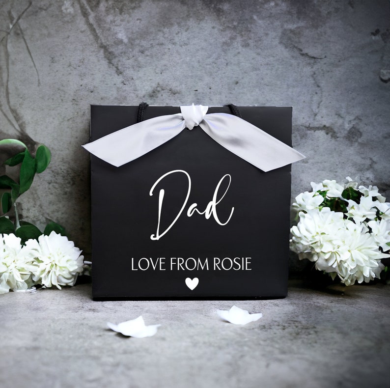 May include: Black gift bag with a white satin ribbon and the words "Dad Love From Rosie" printed on the front.
