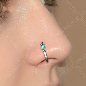May include: A silver nose ring with a turquoise gemstone. The ring is a hoop style with a small decorative detail on the top.
