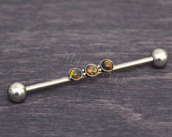 May include: A silver industrial barbell with three round, multicolored opal stones set in the center. The barbell has a ball on each end. The opal stones have a mix of orange, green, and black colors.