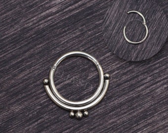 Puede incluir: Anillo de septum de plata con un diseño de doble aro y tres pequeñas cuentas que cuelgan de la parte inferior.