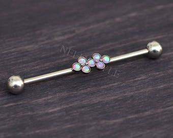 Puede incluir: Un pendiente industrial de barra de plata con un grupo de piedras iridiscentes tipo ópalo. La barra tiene un acabado liso y pulido y extremos esféricos. Las piedras de ópalo están dispuestas en un patrón floral.