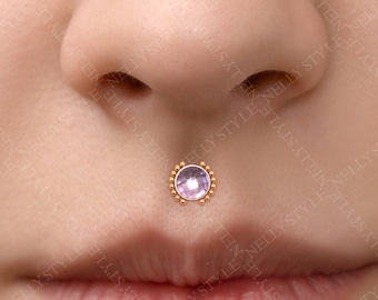 May include: A close-up of a person's lower face with a small purple gem set in a gold lip piercing.