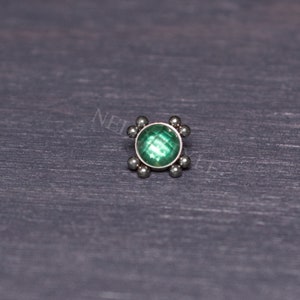 Puede incluir: Una gema verde engastada en un bisel plateado con un borde decorativo de pequeñas bolas plateadas.