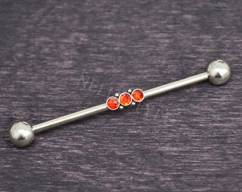 May include: A silver-toned industrial barbell body jewelry piece featuring two smooth spherical end caps and three small, circular, vibrant orange-red gemstones set in a row along the center of the straight metal bar.