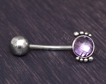 Peut inclure: Un piercing de corps en forme de barre en argent avec une pierre précieuse violette sertie dans une bélière en argent. La pierre précieuse est entourée de petites perles argentées.