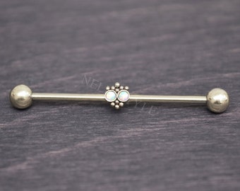 Puede incluir: Barbell de plata con dos piedras de ópalo engastadas en un grupo decorativo. El barbell es una joya de piercing corporal.