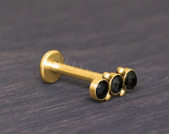 以下が含まれることがあります： 3つの黒い宝石が付いた金のボディピアス。