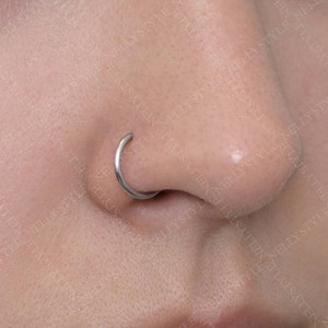 May include: A close-up of a person's nose with a small silver hoop nose ring.