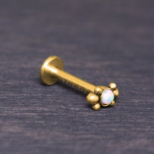 May include: Gold body jewelry with a small opal gemstone and a cluster of small gold balls around the stone.