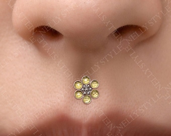May include: A philtrum piercing jewelry piece featuring a flower-shaped design. The center is composed of small silver-toned beads surrounded by six circular, pale yellow gemstones arranged like petals, set in a metallic frame on the skin.
