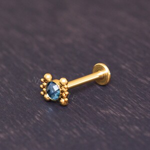 May include: Gold body jewelry with a blue gemstone and a beaded design.